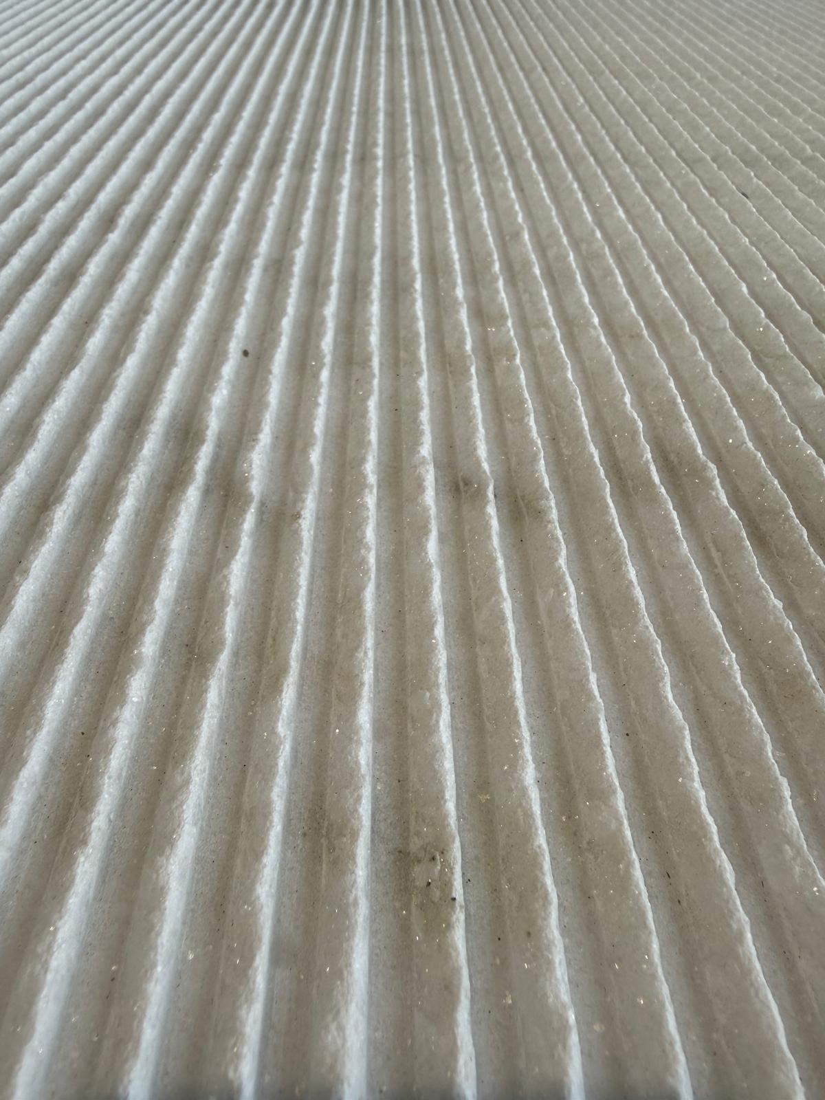 Luce radente su una superficie di pietra scanalata — le ombre nelle scanalature creano profondità e movimento